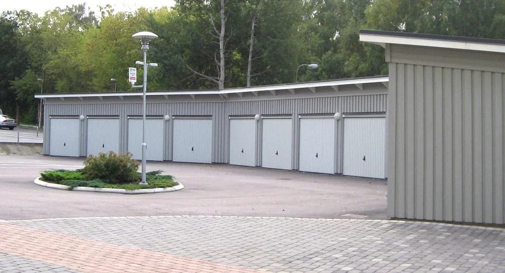 Flera grå garage i en asfalterad uppfart med grönska