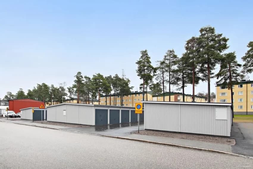 Lagerbyggnader vid en gata i Åby, omgiven av träd.