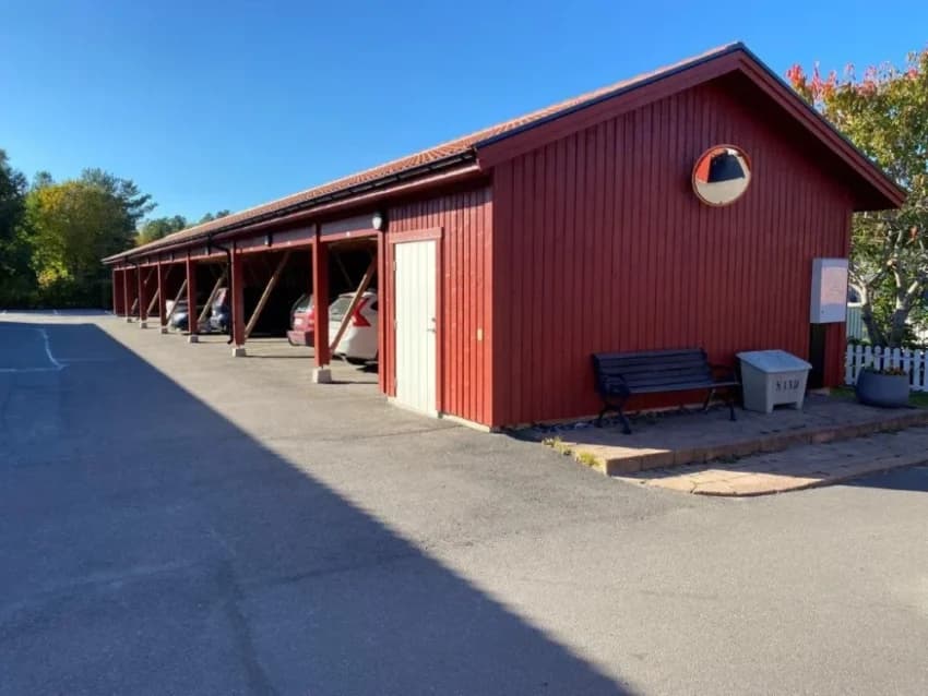 Röd byggnad med parkerade bilar och bänk vid Björkträdet.