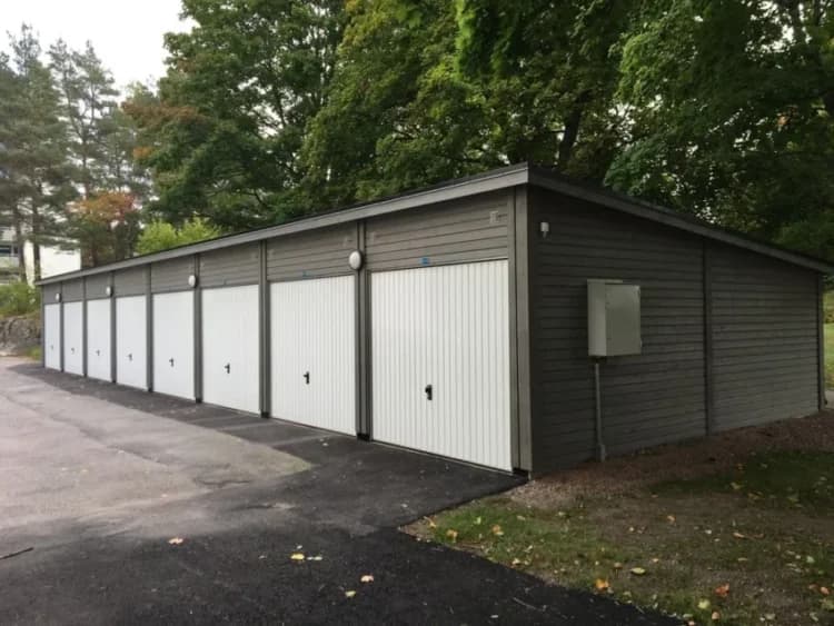 Garage med flera vita dörrar vid Karlavagnsgatan omgiven av träd.