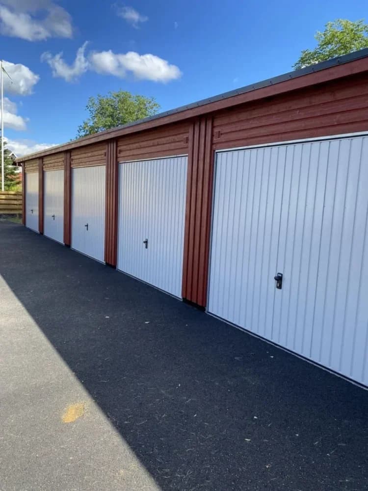 Flera röda garage med vita dörrar och blå himmel.