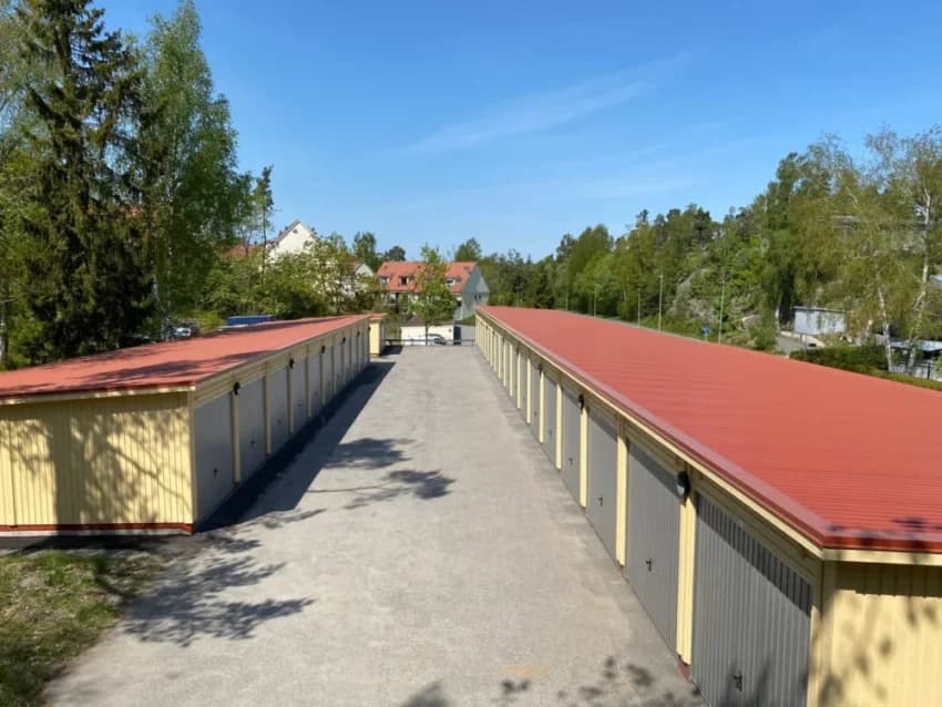 Förrådsbyggnader med röda tak i grönskande omgivning.